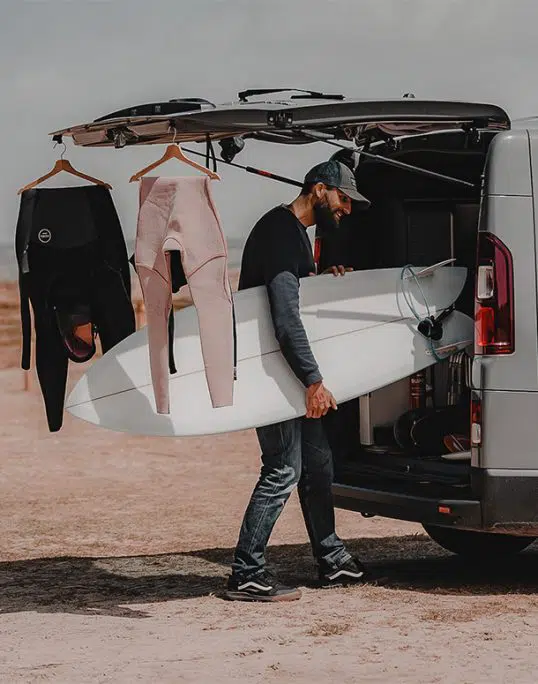 surf stocké dans un coffre de van aménagé hanroad et combinaisons de surf accroché à l'hayon du coffre