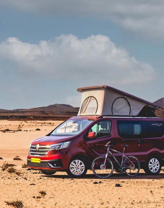 van aménagé hanroad de couleur rouge avec un vélo devant garé dans sur le sable