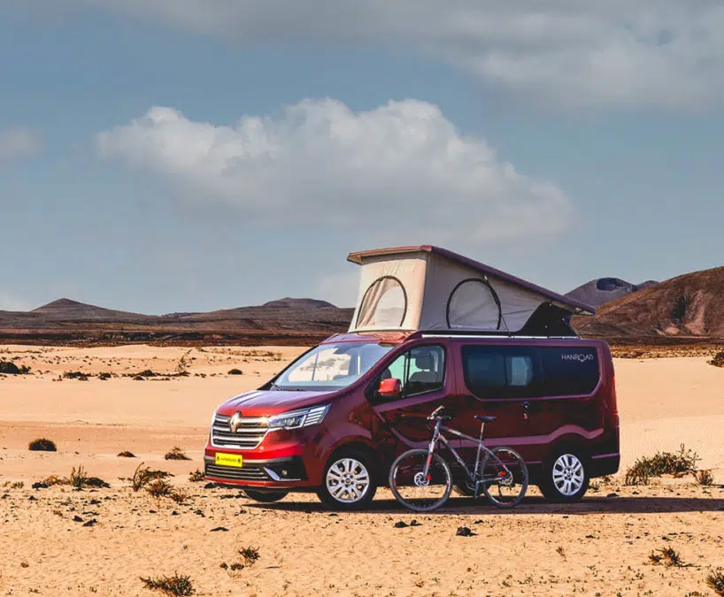 van aménagé hanroad de couleur rouge avec un vélo devant garé dans sur le sable