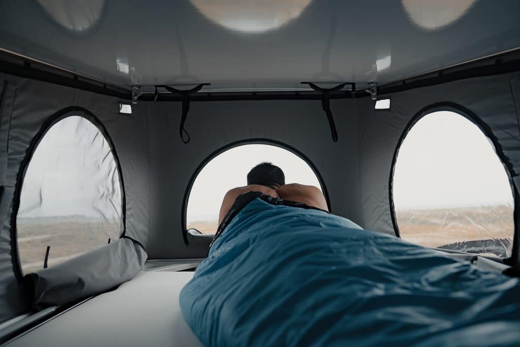 homme dormant dans un lit de toit relevable d'un van aménagé
