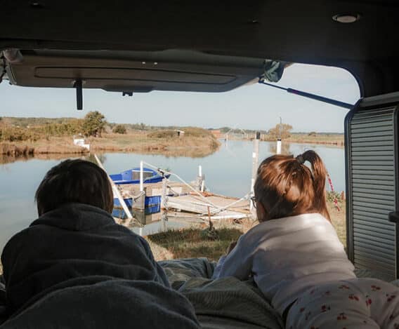deux enfants dormant dans un van aménagé hanroad avec le coffre ouvert sur une rivière