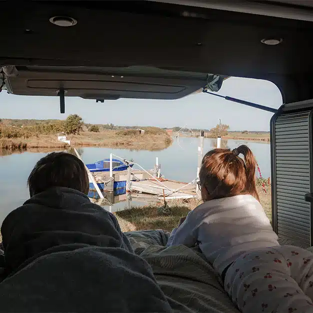 deux enfants dormant dans un van aménagé hanroad avec le coffre ouvert sur une rivière