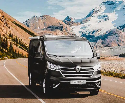 van hanroad de coloris noir roulant sur une route entourée de montagnes enneigées