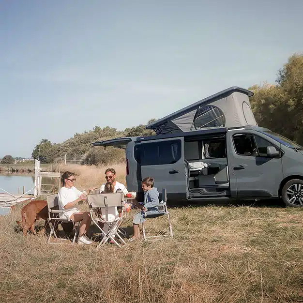 une famille déjeunant devant leur van aménagé sur une table