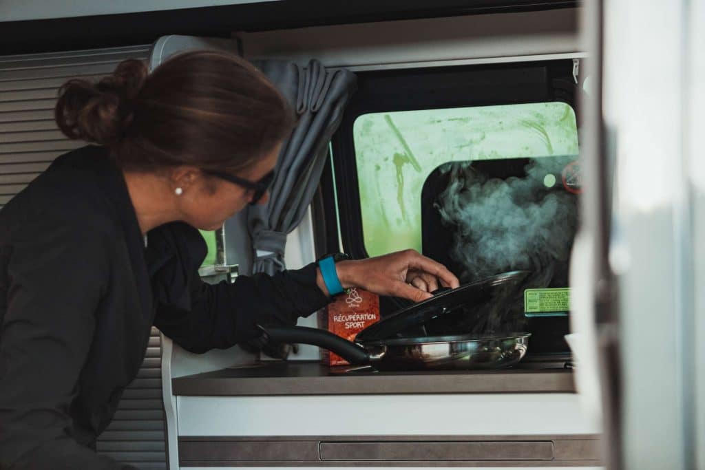 une femme cuisinant dans un van aménagé
