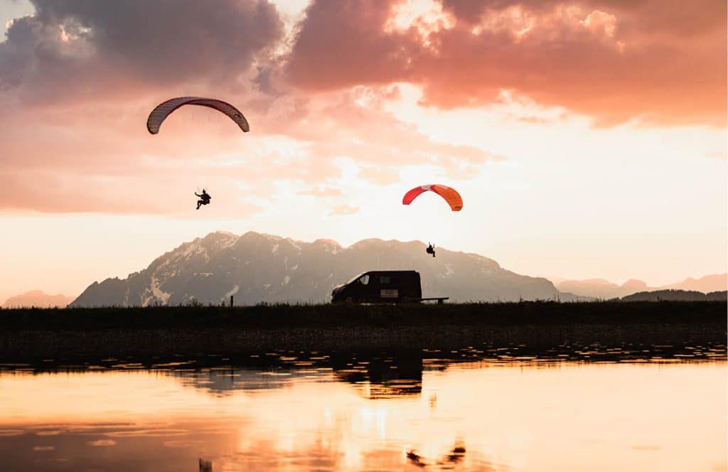 deux parapentistes volant au dessus d'un lac dans un paysage montagneux
