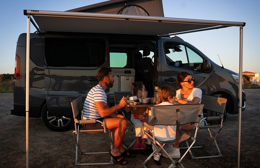 famille avec deux enfants mangeant sur une table devant leur van aménagé hanroad sous un store