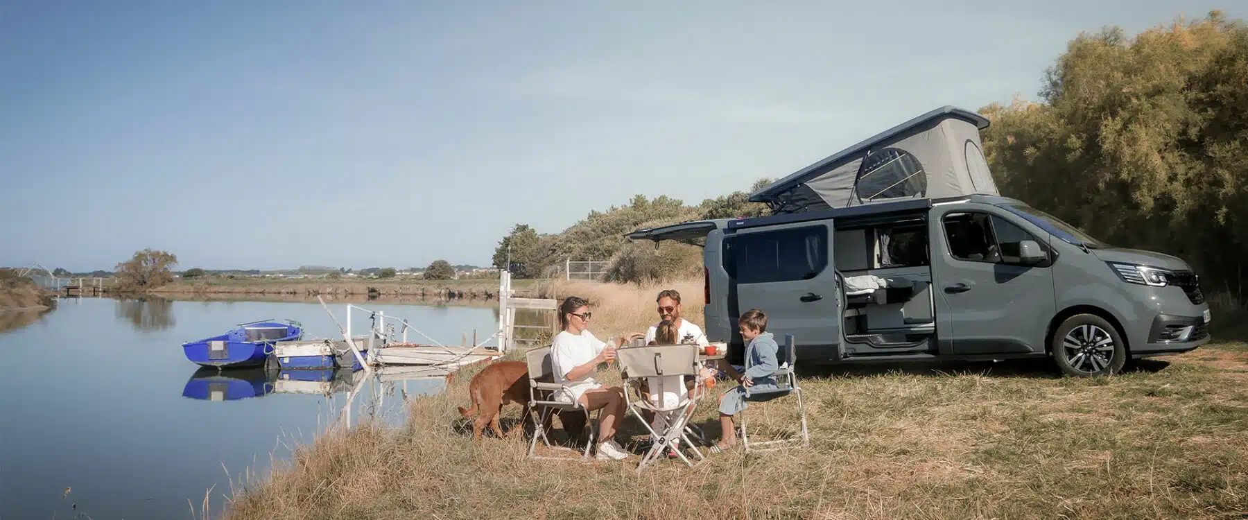 famille de quatre personnes au bord d'une rivière profitant de ses vacances en van aménagé