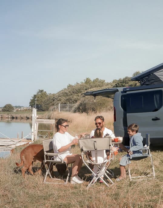 famille de quatre personnes au bord d'une rivière profitant de ses vacances en van aménagé