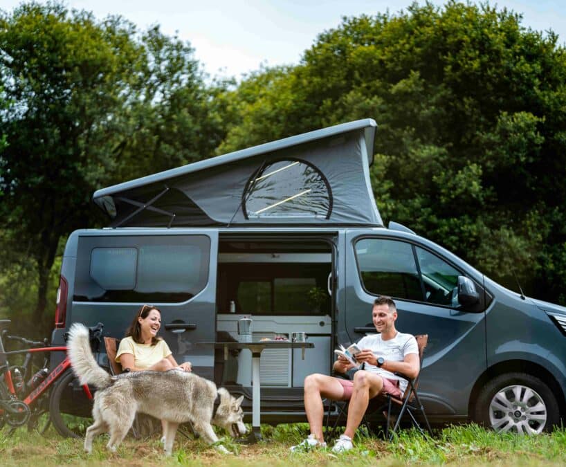 un couple avec chien mangeant devant leur van aménagé