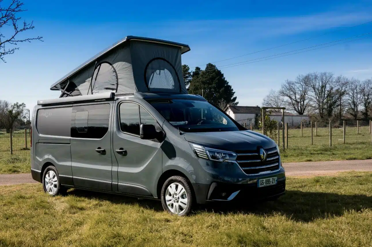 van aménagé sur base renault trafic avec toit relevable, couleur gris urbain, garé sur de l'herbe.