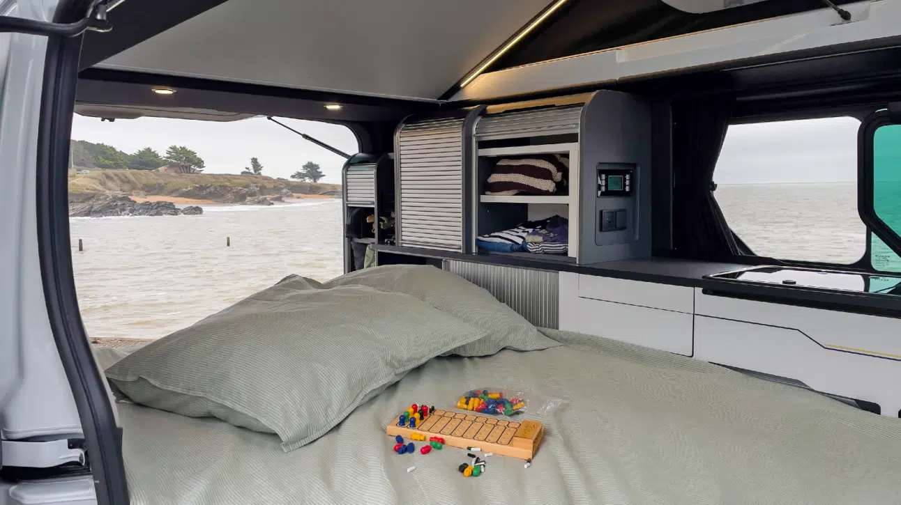 Banquette coulissante en configuration nuit dans le van aménagé avec vue sur la mer.