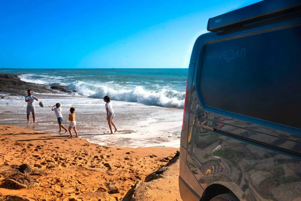 Van aménagé Hanroad avec une famille jouant sur la plage au second plan.