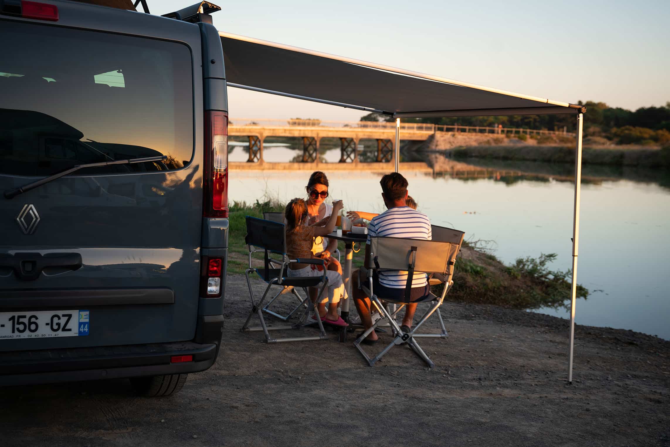 Famille en plein repas sous le store banne de leur van aménagé Hanroad.