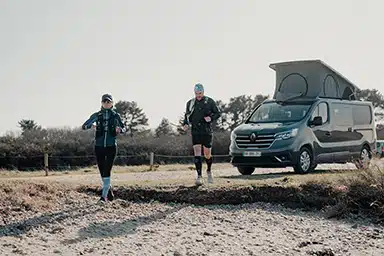 Couple de traileur en pleine sortie trail avec un van aménagé au second plan.