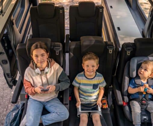 trois enfants assis dans un van aménagé avec leur siège auto